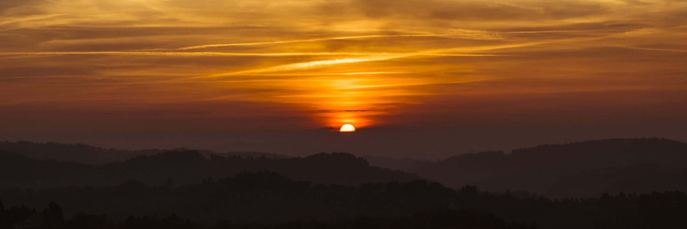 Il sole all'orizzonte tra le colline di Pesaro, sotto nuvole arancioni